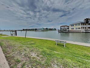 A waterfront property with a grassy area, a bench, a dock, and a building with a thatched roof. - Mermaids Den by Miss Kitty’s (Rockport)