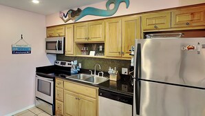 Una cocina con armarios de madera, electrodomésticos de acero inoxidable, salpicadero de azulejos y un letrero que dice 'Keep Calm and Stay Anchored'.