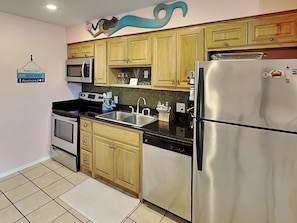 A kitchen with wooden cabinets, stainless steel appliances, a tiled backsplash, and a 'Keep Calm and Stay Anchored' sign. - Mermaids Den by Miss Kitty’s (Rockport)