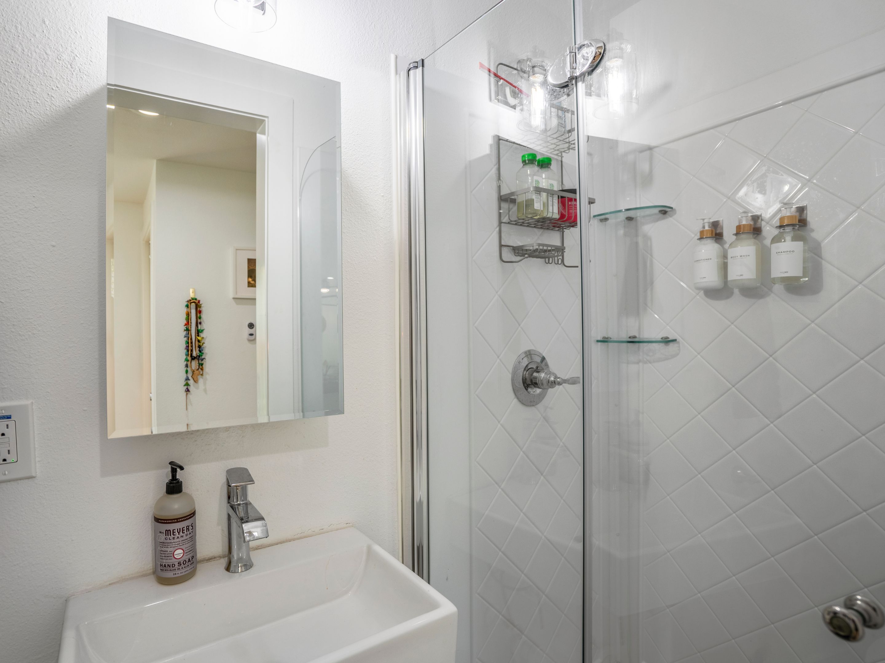 A modern bathroom with a white sink, a mirror, and a glass shower enclosure.