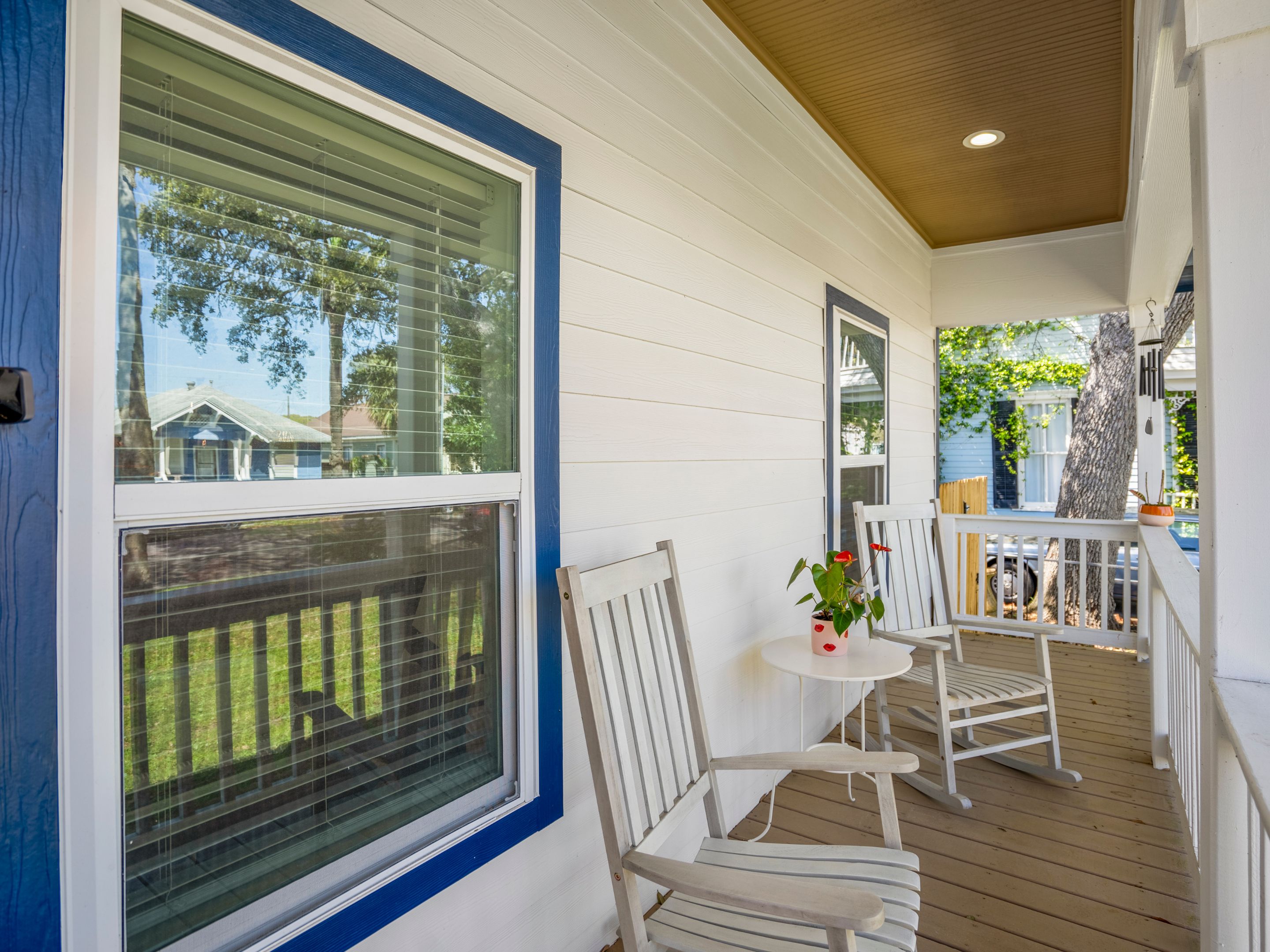 A covered porch with white railings, a small table with a potted plant, and two white chairs.