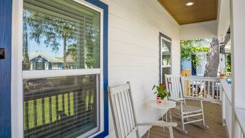 A covered porch with white railings, a small table with a potted plant, and two white chairs.