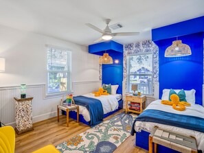A bedroom with two beds, a ceiling fan, and a window with blinds. - Sandy Toes Retreat by Ryson Vacation Rentals (Galveston)