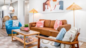 A modern living room with a blue sofa, a brown sofa, and a wooden coffee table with magazines. There are two floor lamps and a painting on the wall.