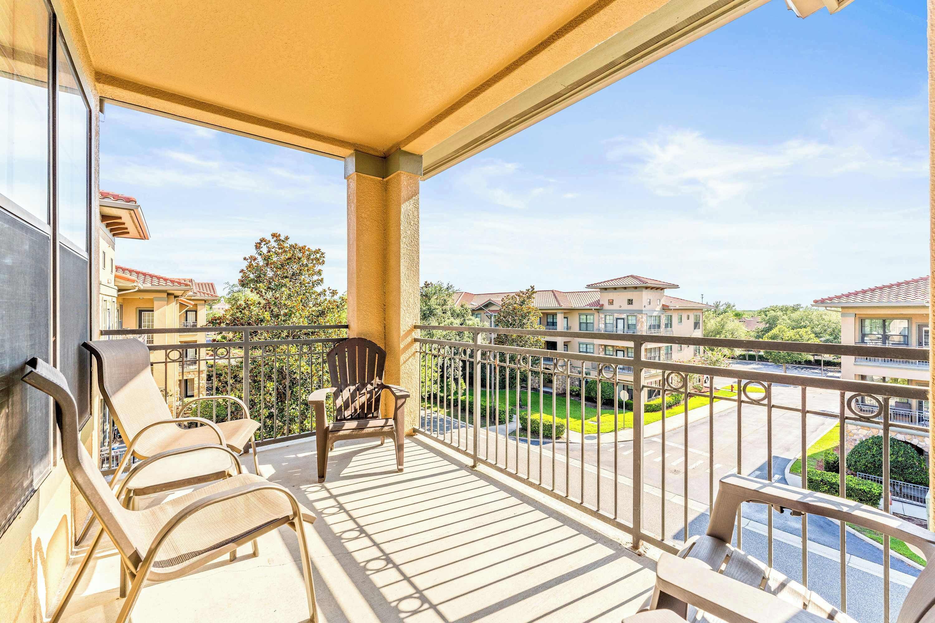 A balcony with two lounge chairs, a small table, and a view of a residential area with houses and a green lawn.