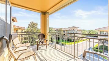 A balcony with two lounge chairs, a small table, and a view of a residential area with houses and a green lawn.