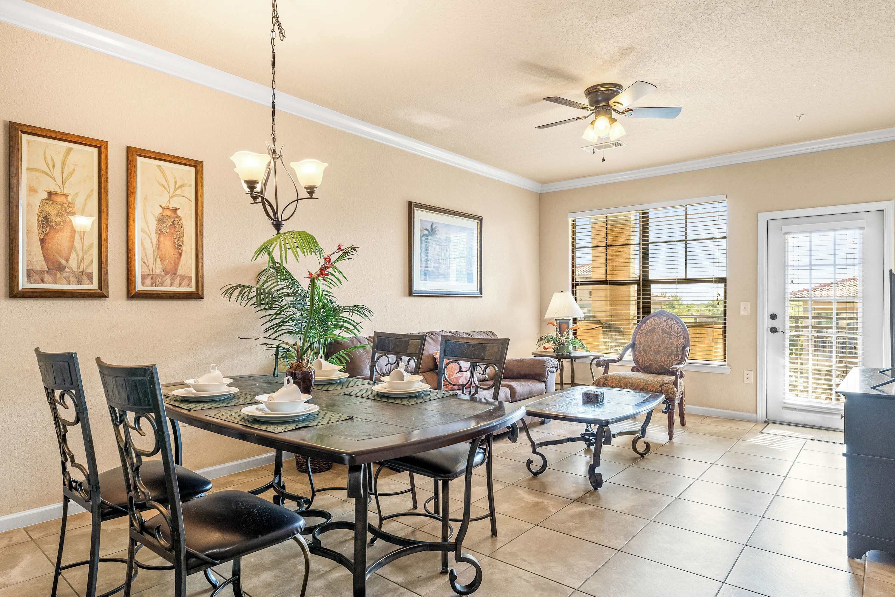 A dining area with a table set for four, surrounded by chairs, a ceiling fan, and a potted plant.