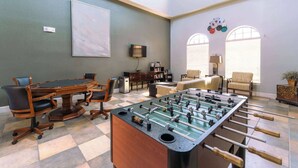 A room with a foosball table, a conference table, and a sofa. There are two windows with blinds, a bookshelf, and a lamp. - Tuscan Paradise At Bella Piazza (Davenport)
