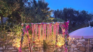 A garden with a stone wall and a swing set decorated with pink flowers. - Alegria Apartments (Paxos)