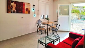 A dining area with a table and chairs, a glass coffee table, a red sofa, and a painting on the wall. - Alegria Apartments (Paxos)