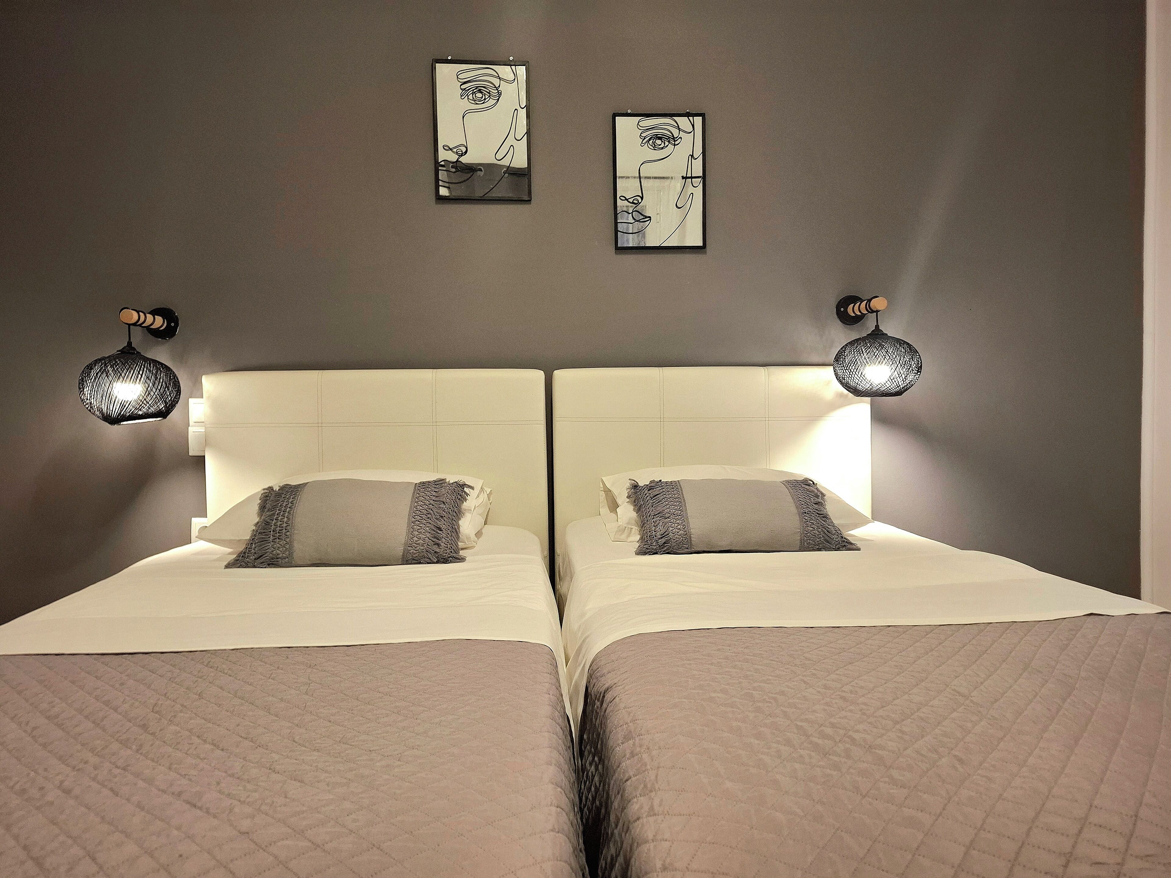 Habitación de hotel con dos camas, cada una con cabecero blanco y colcha acolchada. Hay dos lámparas de pared a cada lado de las camas.