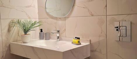 A modern bathroom with a white marble sink, a mirror, a potted plant, and a basket.