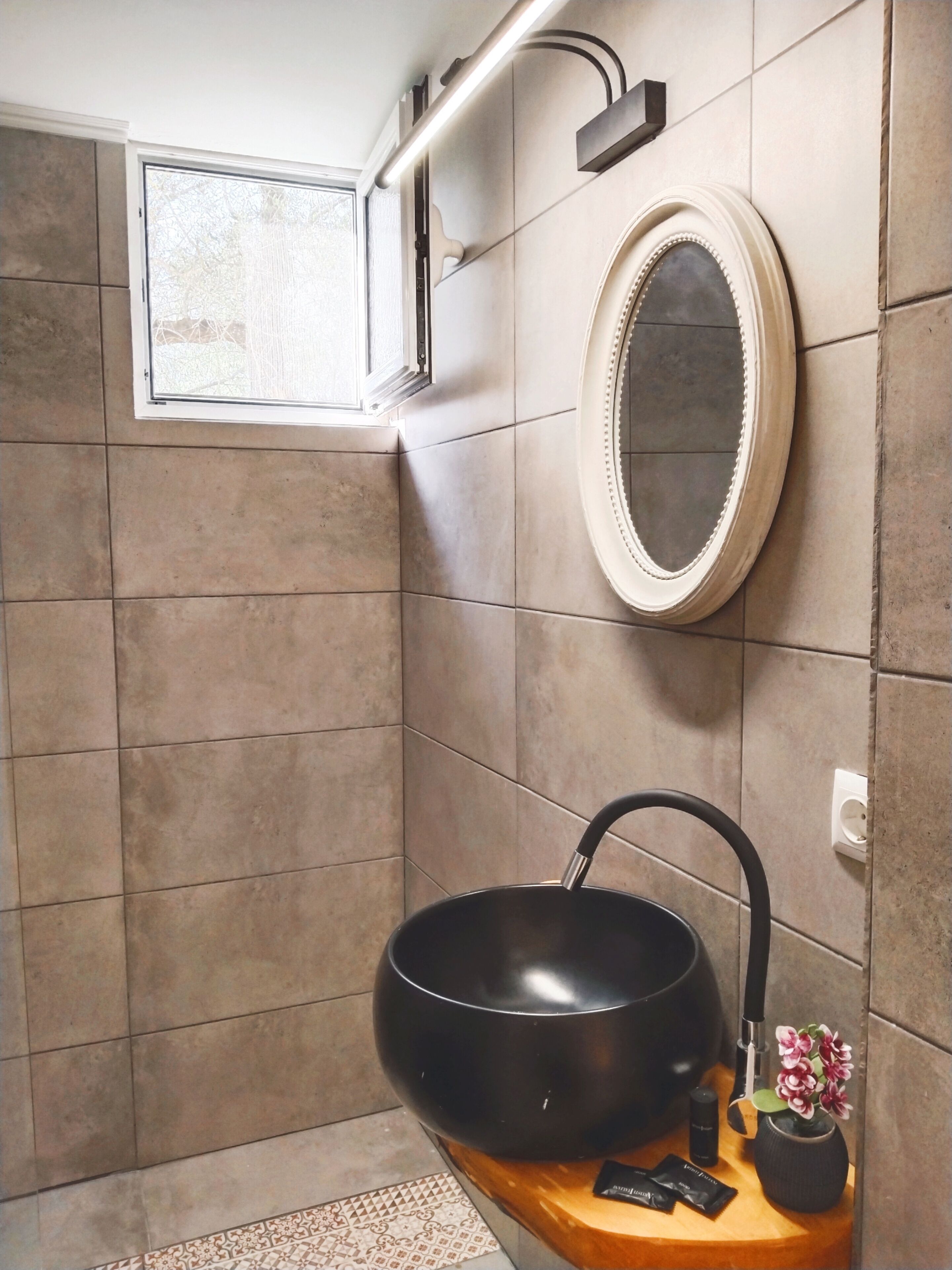 Une salle de bain moderne avec un lavabo noir, un miroir rond et une petite plante en pot.