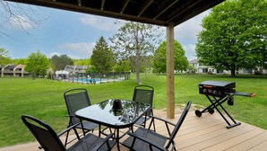 Eine überdachte Terrasse mit einem Glastisch, Stühlen, einem Grill und einem Pool im Hintergrund.
