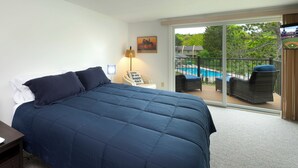 Ein Schlafzimmer mit einem großen Bett, einem Nachttisch, einer Lampe, einem Schild und Blick auf einen Balkon mit Gartenmöbeln und einem Pool.