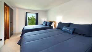 Ein Schlafzimmer mit zwei Betten, einem Fenster mit Vorhängen und Blick ins Grüne.