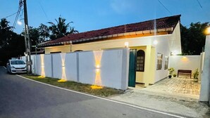 A two-story house with a red-tiled roof, a small porch, and a white fence with lights. - Dream villa and homestay madiha Home (Madiha)
