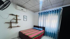 A bedroom with a bed, a ceiling fan, a shelf with items, and a window with curtains. - Dream villa and homestay madiha Home (Madiha)