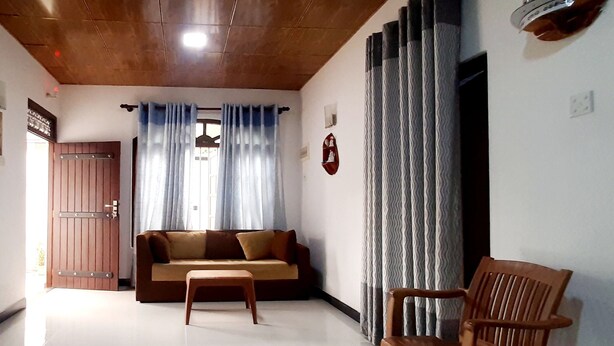 A living room with a sofa, a wooden chair, a blue rug, and a wooden door. - Dream villa and homestay madiha Home (Madiha)