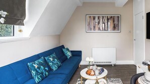 A modern living room with a blue sofa, a coffee table, and a flat-screen TV mounted on the wall.