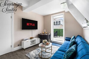 A living room with a blue sofa, a white entertainment unit, a round coffee table, and a TV mounted on the wall displaying "NETFLIX".