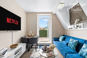 Een woonkamer met een televisie, een blauwe bank, een eettafel en uitzicht op buiten.