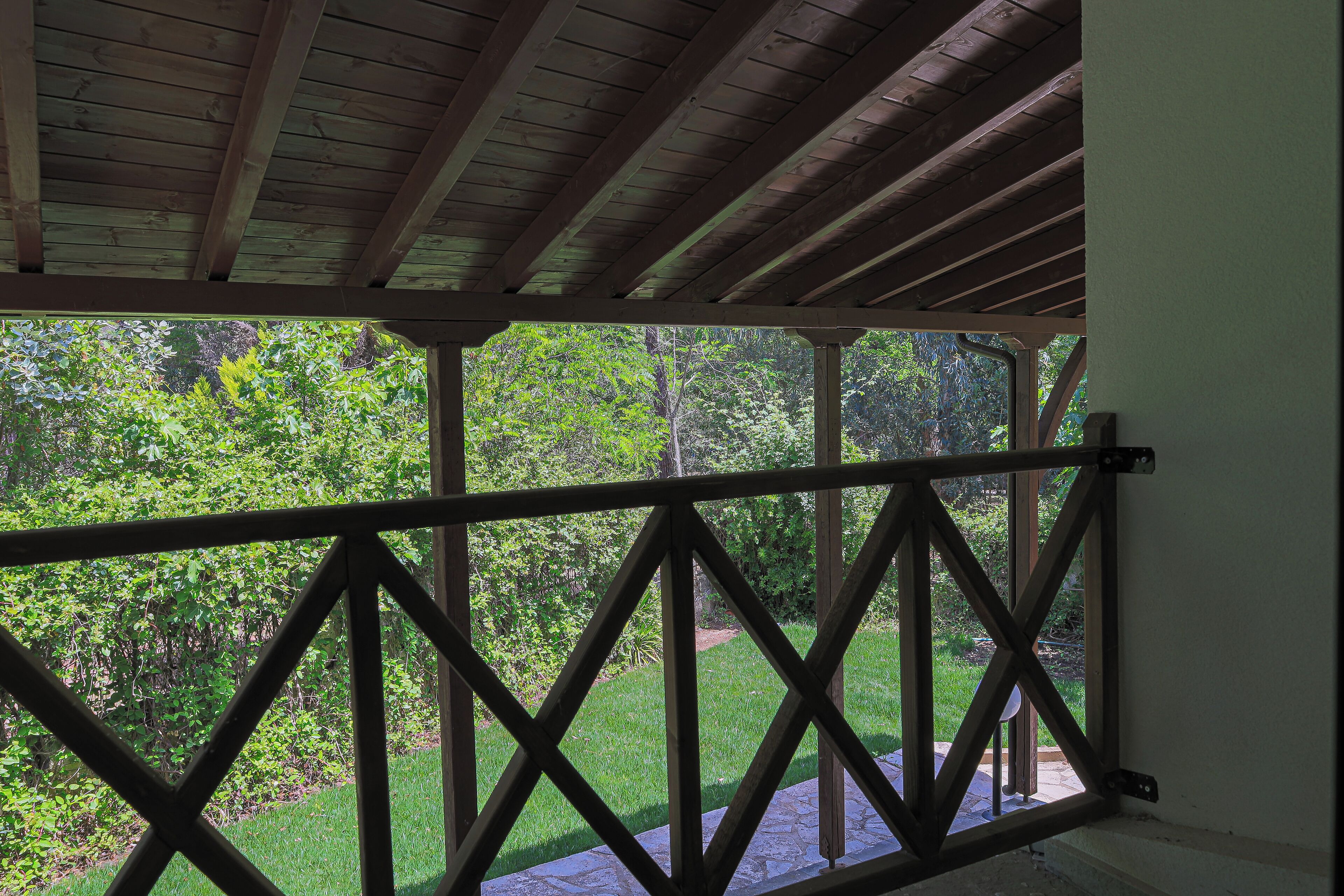 A wooden balcony with a view of a lush garden and a stone pathway.
