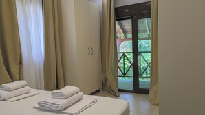 Une chambre d’hôtel avec un lit, une armoire et une vue sur la verdure, visible à travers une porte vitrée.