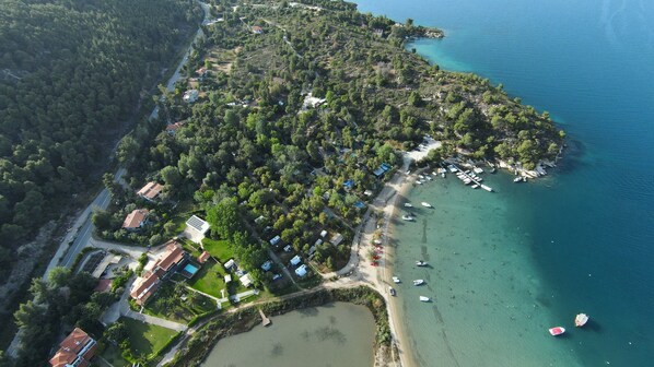 An aerial view of a coastal area with a small beach, boats, and a dense cluster of buildings. - Rea Villa, Vourvourou (Vourvourou)