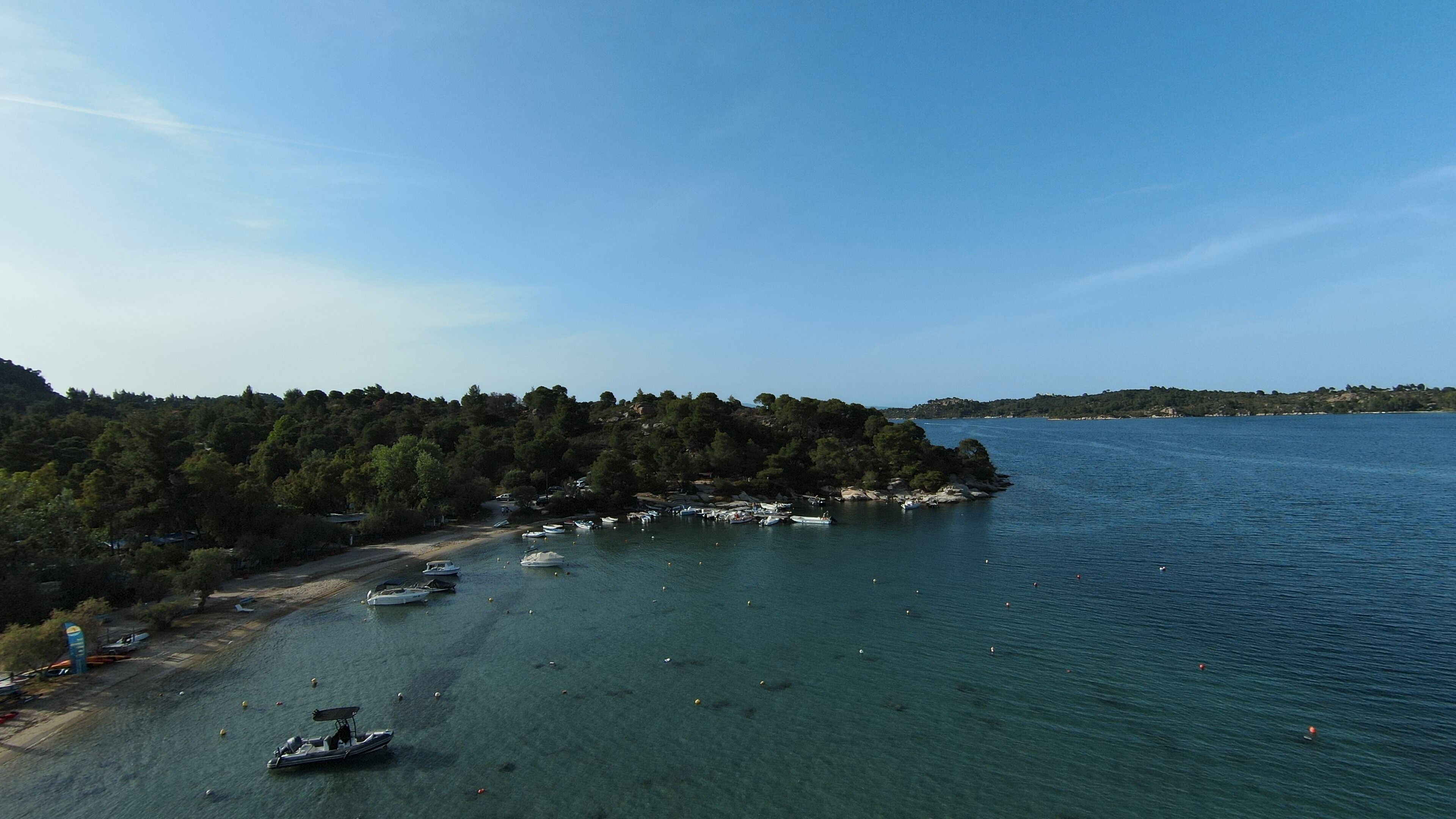 Zona costera con barcos amarrados a la orilla, rodeada de un bosque denso y agua azul cristalina.