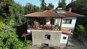 A two-story house with a tiled roof, a balcony with wicker furniture, and a stone facade. - Rea Villa, Vourvourou (Vourvourou)