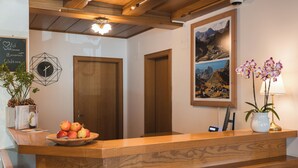 A reception desk with a wooden finish, a framed landscape painting above it, and a clock on the wall. - Smart Hotel Firn (Senales)