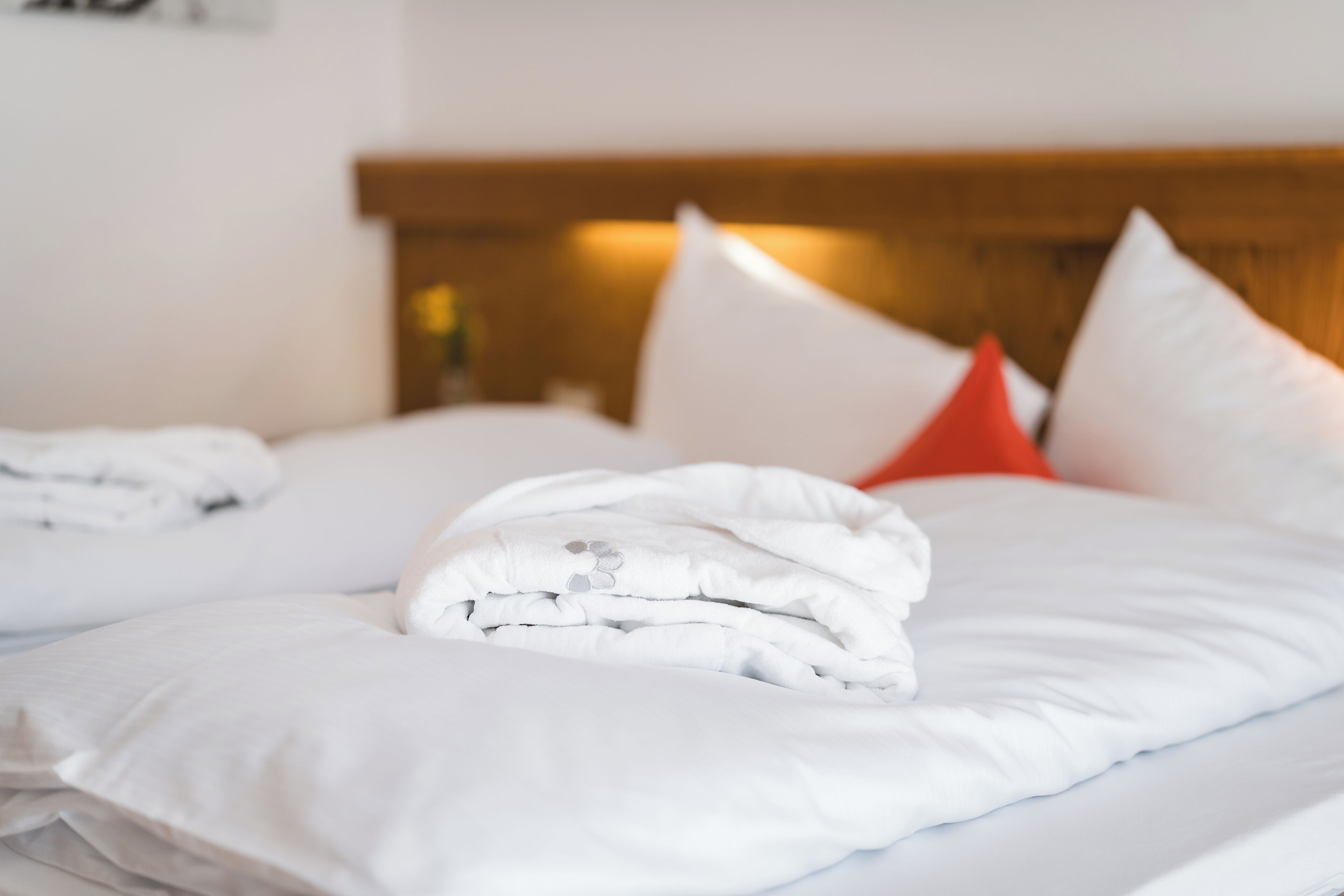 A neatly made bed with white bedding and a red pillow.