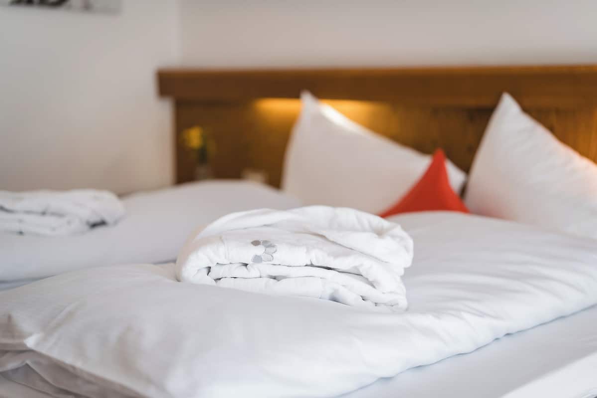 A neatly made bed with white bedding and a few pillows, including a red one.