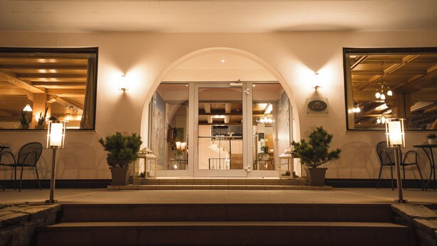 A building entrance with a glass door, steps, and potted plants. - Smart Hotel Firn (Senales)