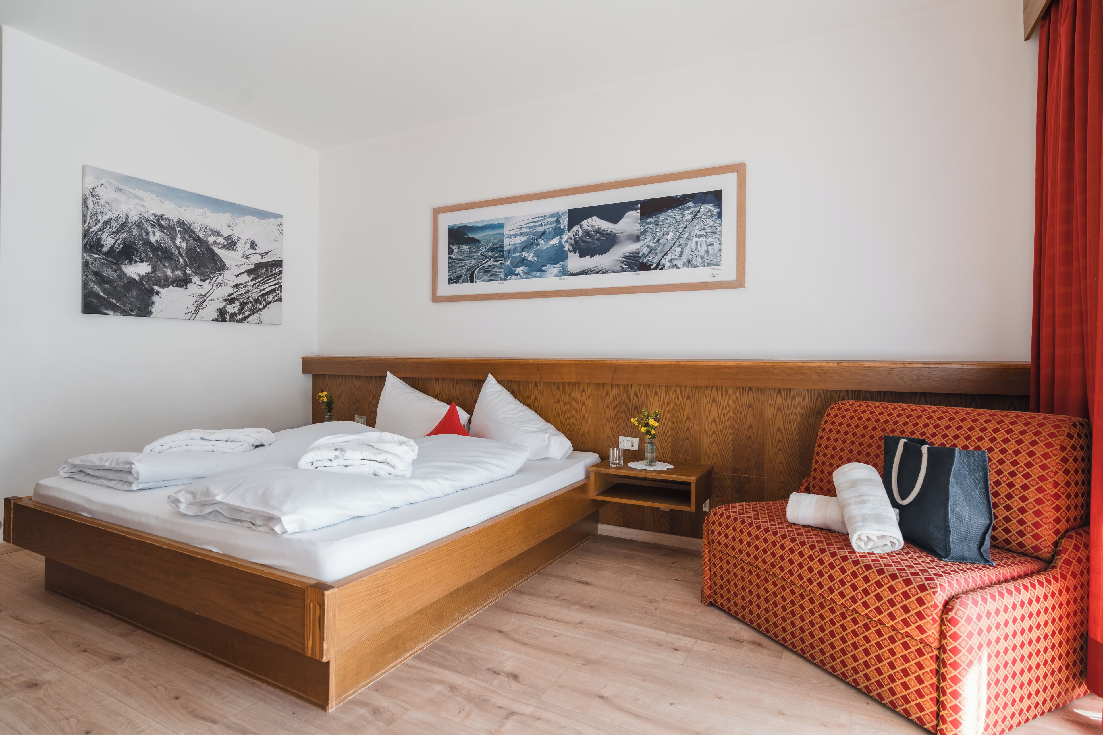 A hotel room with a wooden bed, a red patterned sofa, and two framed photographs on the wall.