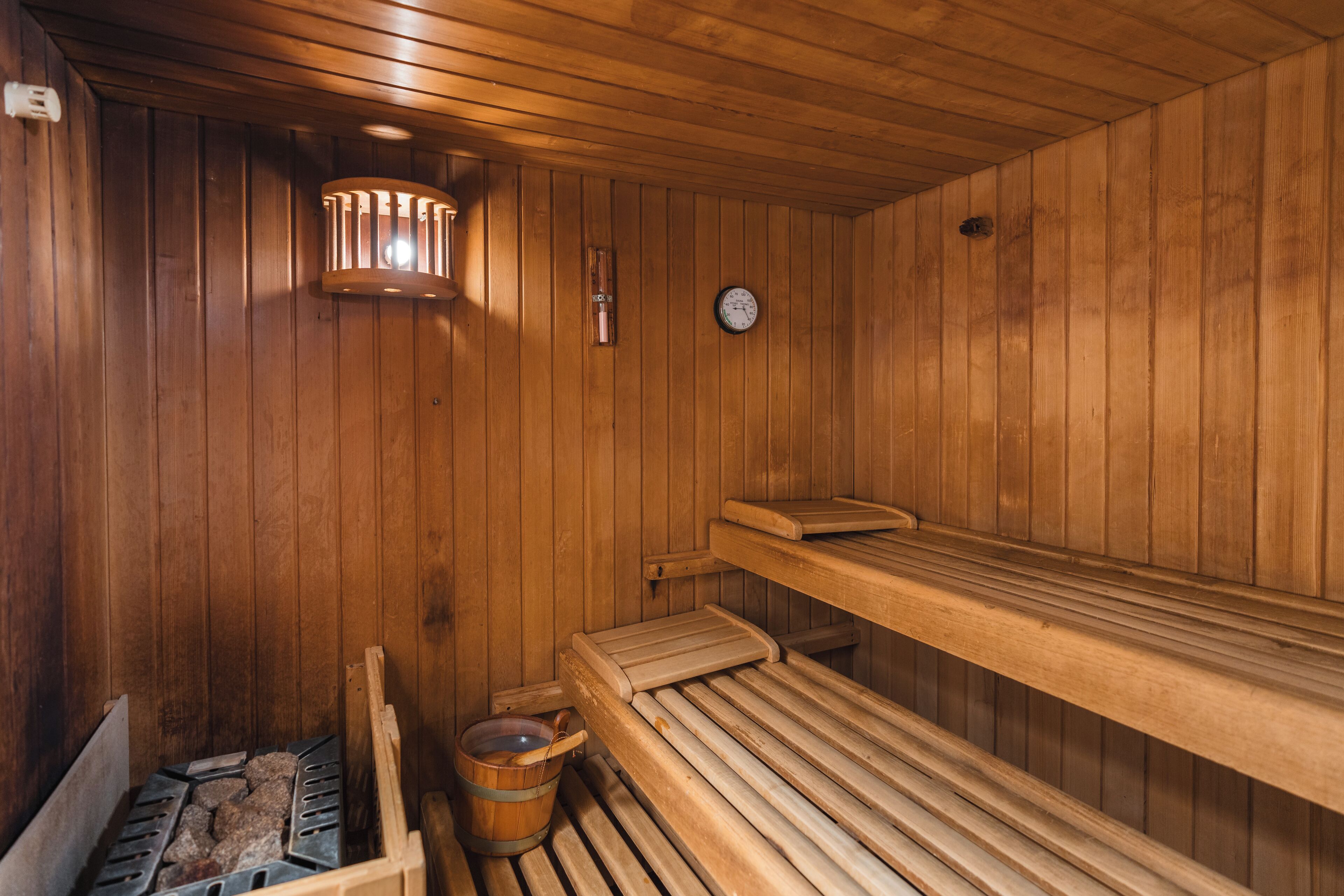 A wooden sauna with benches, a bucket, and a clock on the wall.