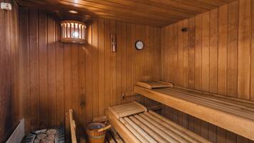 A wooden sauna with benches, a bucket, and a clock on the wall.