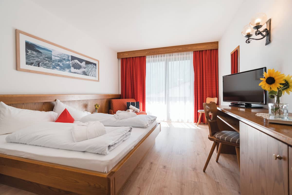 A hotel room with a bed, a desk, a TV, and a window with red curtains.