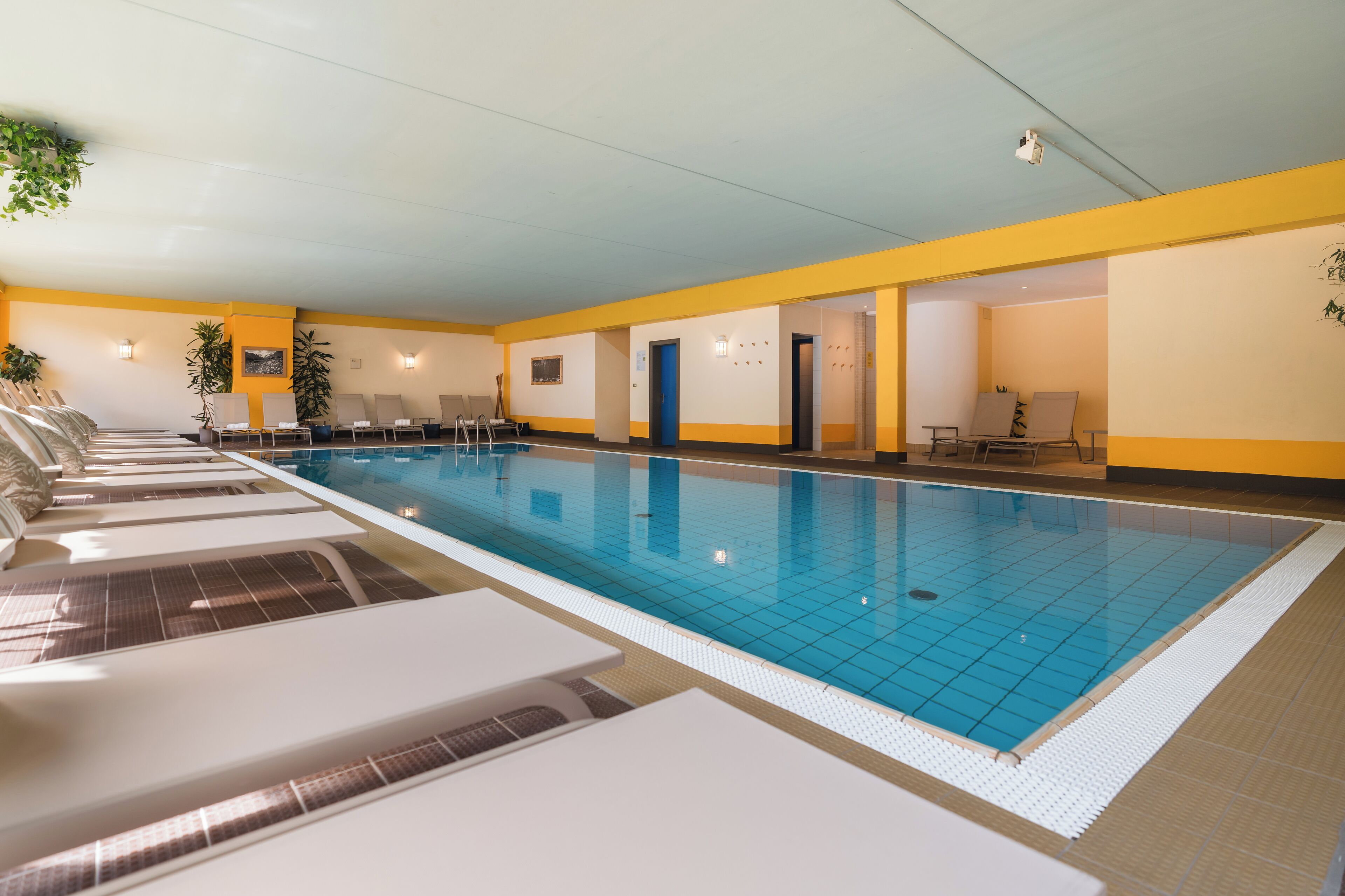 En swimmingpool med liggestole og en dør til et andet rum.
