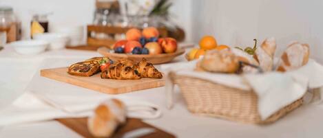Une table mise pour le petit-déjeuner, avec des croissants, du pain et un panier de fruits.