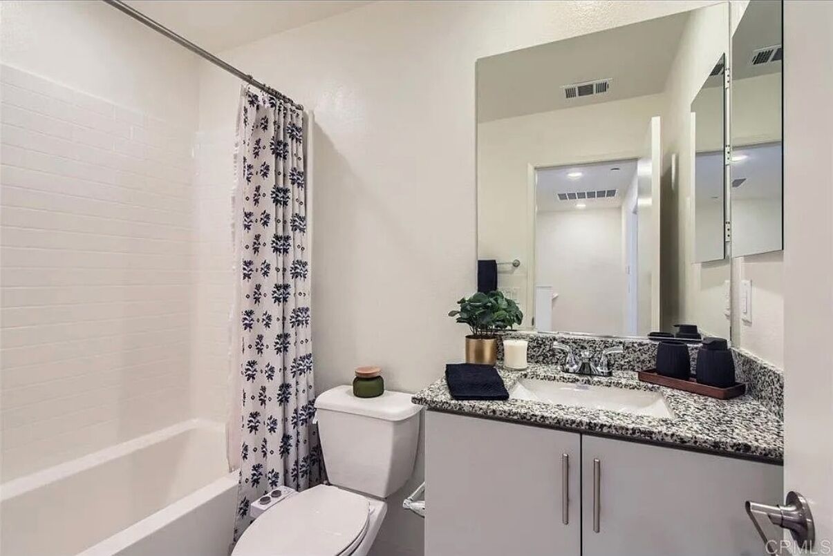 A bathroom with a white bathtub, a toilet, a sink with a granite countertop, and a large mirror.