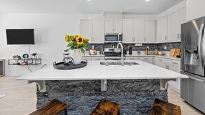 A modern kitchen with a central island, stainless steel appliances, and a flat-screen TV mounted on the wall. - Charming townhome with WiFi, AC, Pool and Community Center in Peaceful Fallbrook (Fallbrook)