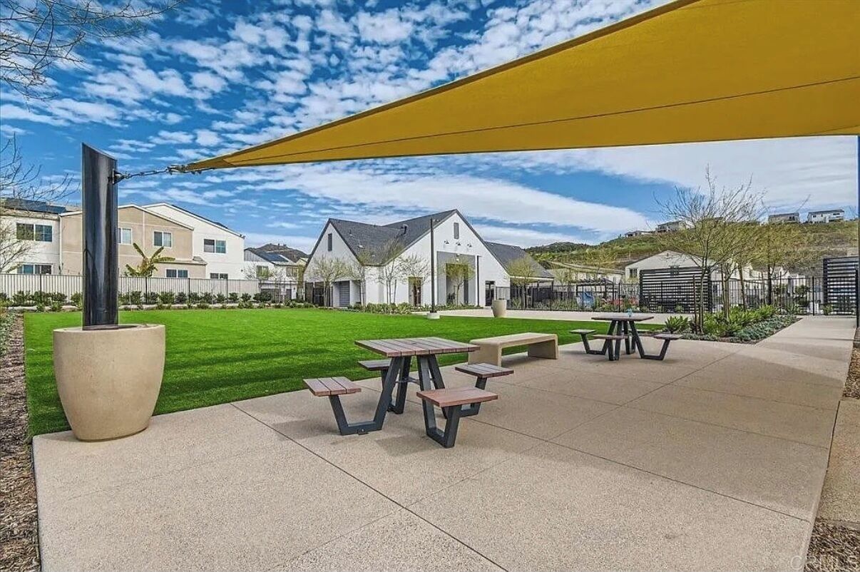 A courtyard with picnic tables, a large planter, and a yellow shade sail.