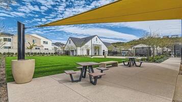 A courtyard with picnic tables, a large planter, and a yellow shade sail.
