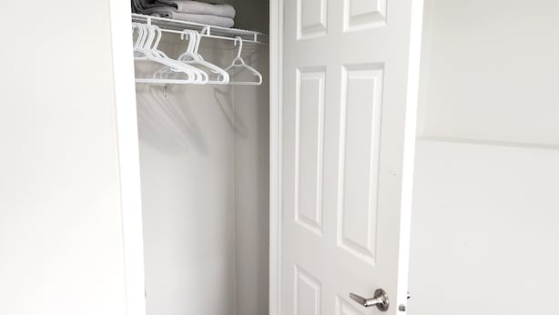 Ein Zimmer mit einer weißen Tür, einem Schrank mit weißen Kleiderbügeln und einem grauen Teppich.