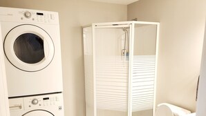 Ein kleines Badezimmer mit Waschmaschine, Duschkabine und Toilette.