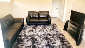 Ein Wohnzimmer mit einer schwarzen Ledersofa, einem gemusterten Teppich und einer TV-Konsole.