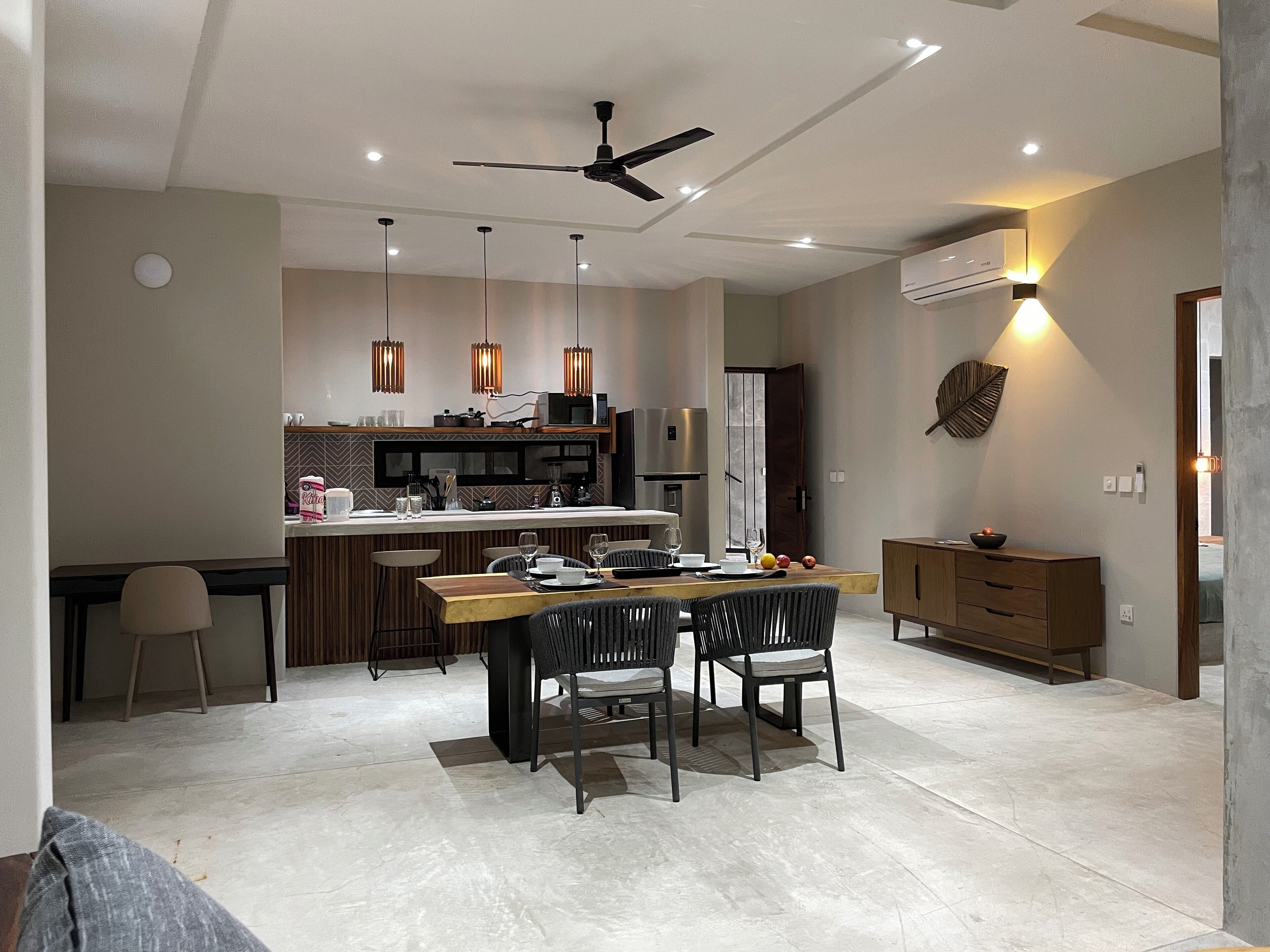 A modern kitchen with a central island, pendant lighting, and a ceiling fan.