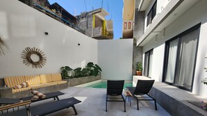A modern outdoor seating area with a pool, lounge chairs, and a sun lounger. - Rooms Zicatela (Puerto Escondido)